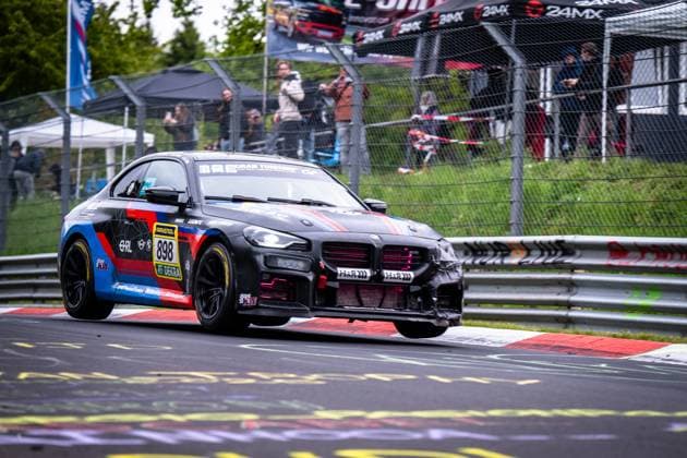 The BMW M2 898 womens national soccer team Finland from Hofor Racing by Bonk Motorsport takes a corner on the Nordschleife of the Nürburgring at the ADAC RAVENOL 24h Nürburgring 2026 The black, blue and red vehicle with the sponsors RAVENOL, H R and DEKRA stands out slightly on the characteristic red and white curb In the background, numerous spectators follow the race action behind the catch fence BMW M2 898 from Hofor Racing by Bonk Motorsport on the Nordschleife Copyright: xMichaelxGelhardtx