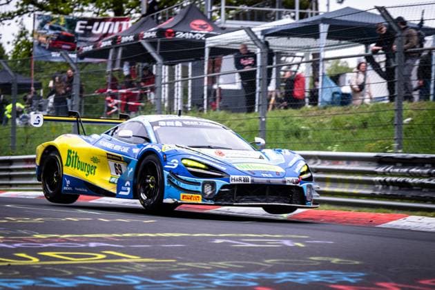 The McLaren GT3 Ben Doerr Marvin Kirchhöfer Timo Glock Timo Scheider Doerr Motorsport from Doerr Motorsport dynamically takes a curb on the Nordschleife at the Nürburgring with the front axle lowered The vehicle wears the eye-catching blue and yellow Bitburger livery with H R and Pirelli sponsorship In the background, numerous spectators watch the race from the side of the track McLaren GT3 69 from Doerr Motorsport on the Nordschleife Copyright: xMichaelxGelhardtx