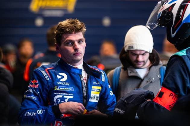 A driver in a blue racing suit with Red Bull and Michelin sponsorship stands in the paddock The racing driver wears the characteristic team clothing with various sponsor logos and is surrounded by other people in the paddock Driver in the paddock at the 24h Nürburgring 2026 Copyright: xMichaelxGelhardtx