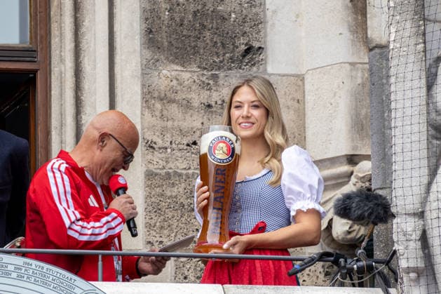 Fußball: Meisterfeier des FC Bayern München auf dem Rathausbalkon und am Marienplatz in München nach dem Gewinn der Bundesliga-Saison 2025 2026. Dame im Dirndl mit übergroßem PAULANER Bier Bierglas (Paulaner Brauererei München) neben Stadionsprecher Stephan Lehmann