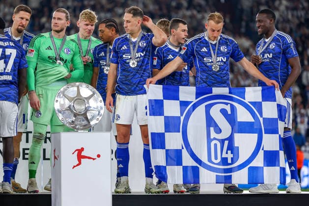 17 05 2026, Fußball, FC Schalke 04 Eintracht Braunschweig, 34 Spieltag, 2 Fußball Bundesliga, Veltins Arena Gelsenkirchen, Saison 2025 2026 Schalke 04 ist Meister der 2 Bundesliga Die Mannschaft gewinnt die Meisterschaft und steht jubilant auf dem Spielfeld Freude und Emotionen nach dem Sieg Timo Becker Schalke04 05 mit der Fahne auf dem Siegerehrungspodest DFB regulations prohibit any use of photographs as image sequences and or quasi video Nordrhein Westfalen Germany