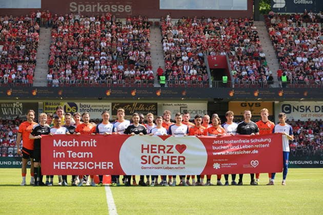 Both teams with the banner Herz Sicher Gemeinsam Leben retten Football Landespokal Brandenburgt 2025 2026 Final FC Energie Cottbus VfB Krieschow 1921