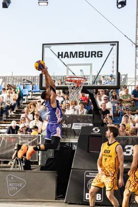 At the FIBA 3x3 Hamburg Challenger in the Active City Arena, a player in a purple jersey shows an impressive dunking attempt to the basket, while players in yellow jerseys of the Barcelona team follow the action The event took place on May 23, 2026 in Hamburg Spectacular dunking moment at the FIBA 3x3 Hamburg Challenger Copyright: xspeedshotx