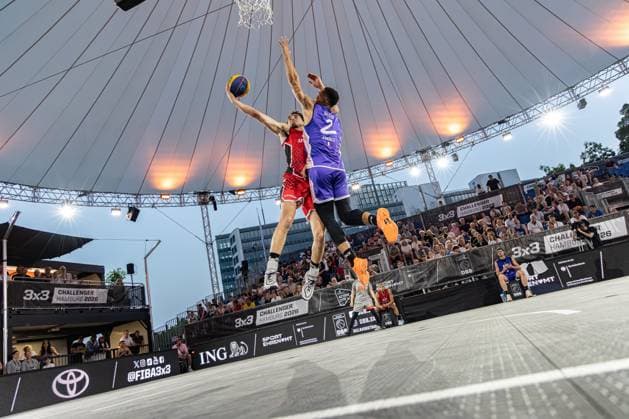 The FIBA 3x3 Hamburg Challenger 2026 in the Active City Arena shows an intense game situation A player in the red jersey attempts a dunk while his opponent 2, Toulouse FRA in the blue jersey, blocks the throw The game takes place under the open sky with an impressive tent roof arena Spectacular dunk attempt against Toulouse in the Active City Arena Hamburg Copyright: xspeedshotx