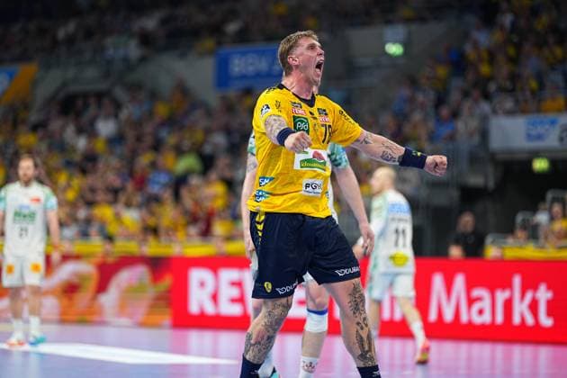Haukur Thrastarson 25 of the Rhein Neckar Löwen cheers with a clenched fist and wide open mouth in the SAP Arena In the background are players from both teams in white and yellow jerseys Haukur Thrastarson 25 Rhein Neckar Löwen celebrates a goal in the SAP Arena Copyright: xspeedshotx