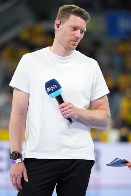 Tobias Reichmann stands on the SAP Arena pitch with a DYN microphone in his hand He wears a white T-shirt and an in-ear headset Tobias Reichmann as DYN presenter in the SAP Arena Copyright: xspeedshotx