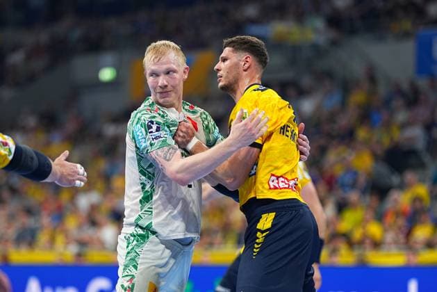 Magnus Saugstrup in the white SC Magdeburg jersey and Sebastian Heymann in the yellow Löwen jersey stand in a physical duel in the SAP Arena Heymann holds Saugstrup while both players make direct physical contact Magnus Saugstrup 23 SC Magdeburg in a duel with Sebastian Heymann 13 Rhein Neckar Löwen Copyright: xspeedshotx
