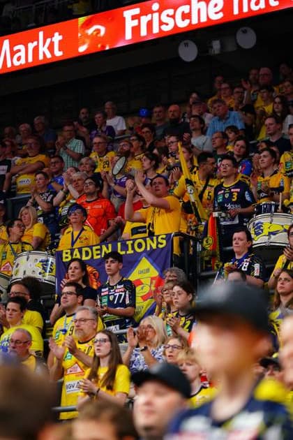 The Rhein Neckar Löwen fan corner is packed with fans in yellow jerseys watching the match A purple banner of the Baden Lions fan club is clearly visible in the block, accompanied by drums from the fan group Rhein Neckar Löwen fans with Baden Lions banner in the SAP Arena Copyright: xspeedshotx