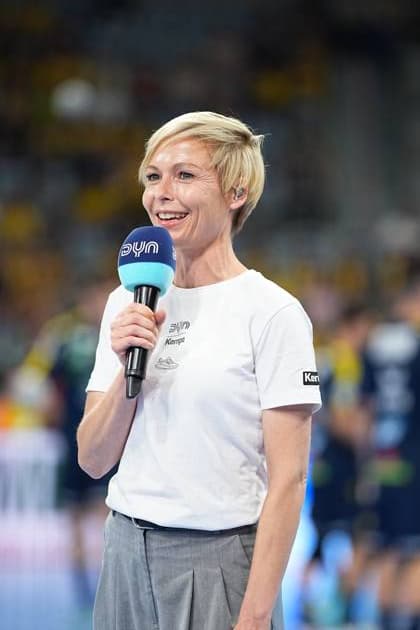 Anett Sattler presents with a DYN microphone in the SAP Arena at the DAIKIN HBL match Rhein Neckar Löwen against SC Magdeburg She wears a white Kempa shirt with DYN logo Presenter Anett Sattler with DYN microphone in the SAP Arena Copyright: xspeedshotx