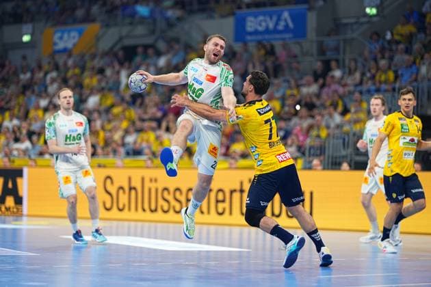 A SC Magdeburg player in the white jersey jumps to throw and is blocked by Dani Baijens 77 in the yellow jersey of Rhein Neckar Löwen Gino Steenaerts 14 Rhein Neckar Löwen can be seen in the background on the right, the SAP Arena is filled with yellow-clad spectators SC Magdeburg player 23 SC Magdeburg throwing against Dani Baijens 77 Rhein Neckar Löwen Copyright: xspeedshotx