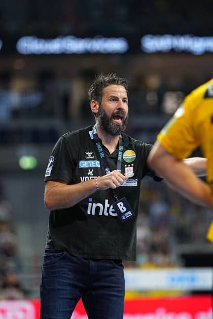 SC Magdeburg coach Bennet Wiegert stands on the touchline in the SAP Arena with his mouth open and gesticulating He wears a dark coachs shirt with the SC Magdeburg emblem and an HBL accreditation badge Bennet Wiegert Coach SC Magdeburg gives instructions on the touchline Copyright: xspeedshotx