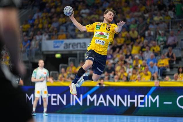 David Möré 15 of the Rhein Neckar Löwen jumps high into the air and takes the shot, the ball in his raised throwing hand A player in a white SC Magdeburg jersey can be seen in the background, the SAP Arena is filled with fans dressed in yellow David Möré 15 Rhein Neckar Löwen taking a jump shot Copyright: xspeedshotx
