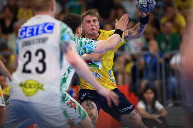 Edwin Aspenbäck 78 Rhein Neckar Löwen in the yellow jersey takes on a Magdeburg defender and takes a shot In the foreground is Magnus Saugstrup 23 SC Magdeburg in the white jersey Edwin Aspenbäck 78 Rhein Neckar Löwen taking a shot against SC Magdeburg Copyright: xspeedshotx