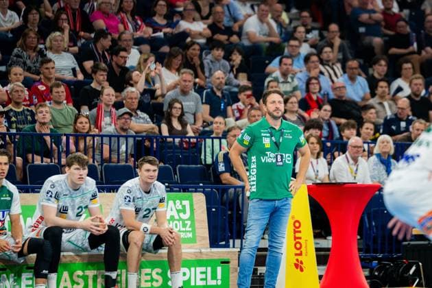 Ben Matschke, coach of Frisch Auf Göppingen, stands on the touchline in a green polo shirt Sascha Brodbeck 21 and Oskar Sunnefeldt 27 sit on the bench in white club shirts Ben Matschke and players from Frisch Auf Göppingen in the Barclays Arena Copyright: xPhilippHeistx