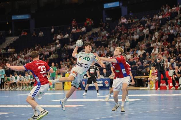 Elias Newel of Frisch Auf Göppingen jumps to shoot with the ball in his right hand while two Hamburg defenders try to block the shot The Barclays Arena is packed and creates an intense atmosphere Elias Newel 40 Frisch Auf Göppingen taking a jump shot against HSV Hamburg Copyright: xspeedshotx