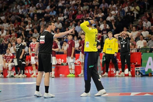 A referee in a black uniform gestures during a break in play In the background, players from both teams stand on the pitch as spectators in the packed Barclays Arena watch Referee during a stoppage in play at Barclays Arena Copyright: xspeedshotx