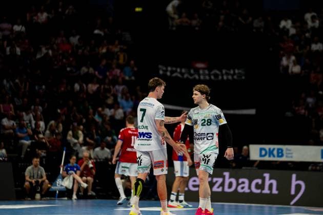 Two Frisch Auf Göppingen players in white jerseys talk during a break in play at the Barclays Arena In the background are spectators and HSV Hamburg players in red jerseys Handball Sport Verein Hamburg vs Frisch Auf Göppingen Copyright: xPhilippHeistx