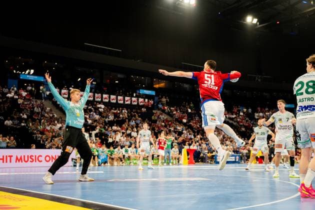 An HSV Hamburg player in red jersey 51 performs a jump shot while a Göppingen player in turquoise goalkeeper jersey forms the defense The scene shows intense attacking action in the Barclays Arena in front of a packed crowd Handball Sport Verein Hamburg vs Frisch Auf Göppingen Copyright: xPhilippHeistx