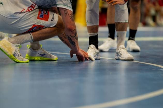 Close-up of players from both teams during an intense game scene on the handball court The shot shows the lower parts of the bodies of several players in white jerseys from Frisch Auf Göppingen and other players, with one players hand touching the ball on the ground Handball Sport Verein Hamburg vs Frisch Auf Göppingen Copyright: xPhilippHeistx