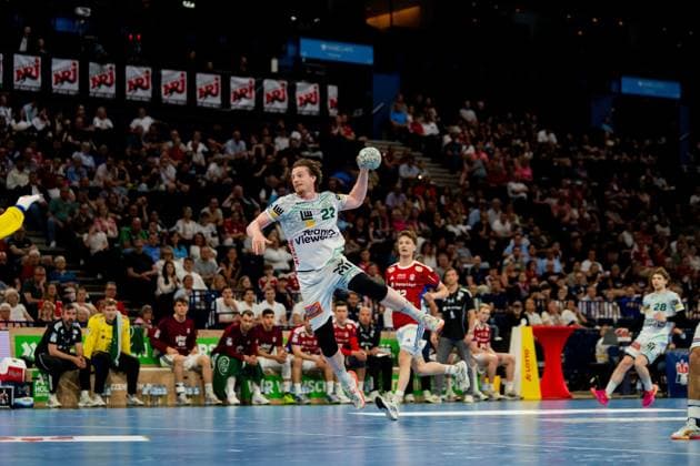 Erik Persson jumps for the goal throw and holds the ball in the air In the background are spectators of the Barclays Arena and players of both teams Handball Sport Verein Hamburg vs Frisch Auf Göppingen Copyright: xPhilippHeistx