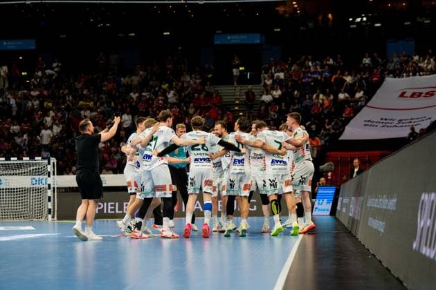 The Frisch Auf Göppingen team forms a circle on the pitch to celebrate a win during the Bundesliga match against HSV Hamburg at Barclays Arena The players in white jerseys embrace in the center of the pitch as spectators watch the action in the background Handball Sport Verein Hamburg vs Frisch Auf Göppingen Copyright: xPhilippHeistx