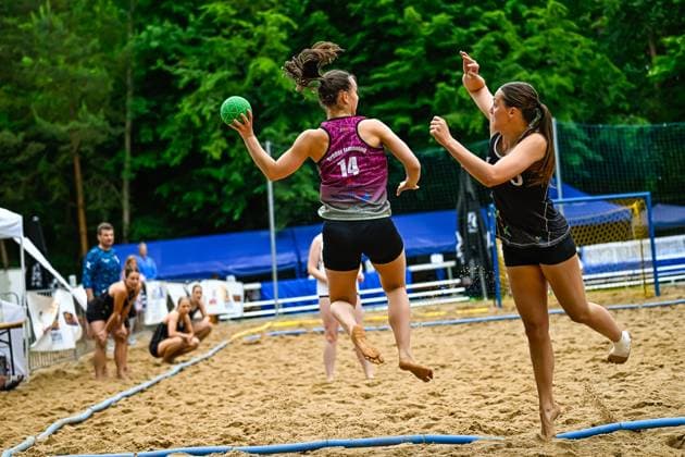 A player from Brüder Ismaning 14 jumps off and takes a throw while an opponent in a black jersey tries to block the throw The game takes place on an outdoor sand court Player 14 Brüder Ismaning attempting a throw in beach handball Copyright: xspeedshotx xDorianfrickx