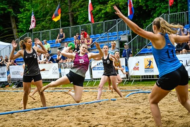 A player with jersey number 15 jumps to throw on the sand field at the Karacho Beach Cup Two players with NED print 2 and 9 as well as an opponent 11 can be seen in the picture Player 15 throwing at the Karacho Beach Cup Copyright: xspeedshotx xDorianfrickx