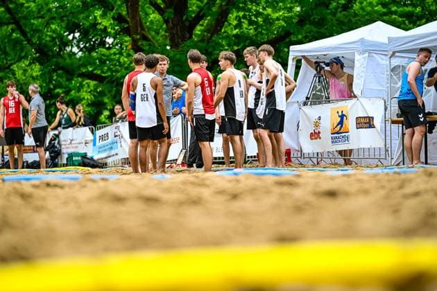 Several players of the German youth national team stand together on the sandy field at the Karacho Beach Cup, recognizable by the jerseys with GER print and the numbers 5, 6 and 8 In the background are advertising boards, a cameraman and the tournament tent Germany juniors at the Karacho Beach Cup in team talk Copyright: xspeedshotx xDorianfrickx