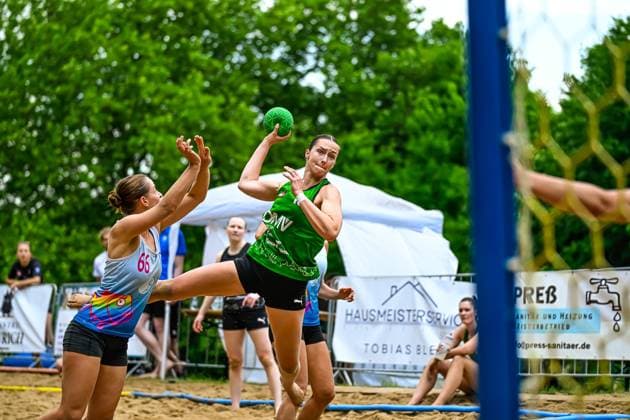 A player in the green jersey takes a shot from a jump, while player 66 in the colored jersey tries to defend The game takes place on an outdoor sand court Throwing action in beach handball Player in the green jersey takes a shot Copyright: xspeedshotx xDorianfrickx