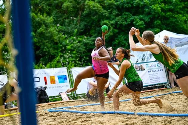 A player in a pink jersey jumps to throw and is put under pressure by two opponents in green jerseys The game takes place on an outdoor sand court Throwing action at a beach handball tournament in the sand Copyright: xspeedshotx xDorianfrickx