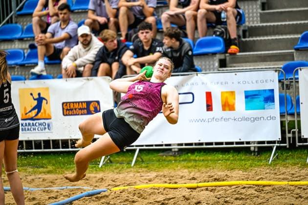 A player in a magenta jersey throws herself across the sand court in a dynamic jump shot at the Karacho Beach Cup German Beach Open Spectators in the stands watch the action in the background Spectacular jump shot at the German Beach Open Karacho Beach Cup Copyright: xspeedshotx xDorianfrickx