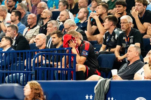 An MT Melsungen player sits on the substitutes bench and buries his face in a red jersey, surrounded by spectators and team officials The posture expresses disappointment or exhaustion MT Melsungen vs SG Flensburg Handewitt - EHF Finals Hamburg 2026 Copyright: xPhilippHeistx