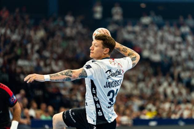 Emil Jakobsen 31 SG Flensburg Handewitt takes a shot with the ball in his raised throwing hand and jumps in the process A well-filled grandstand can be seen in the background MT Melsungen vs SG Flensburg Handewitt - EHF Finals Hamburg 2026 Copyright: xPhilippHeistx