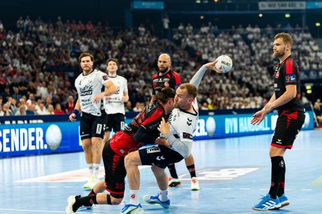 Johannes Golla 3 SG Flensburg Handewitt gets the better of an MT Melsungen defender and throws on goal In the background, other players from both teams watch the scene in front of a full crowd MT Melsungen vs SG Flensburg Handewitt - EHF Finals Hamburg 2026 Copyright: xPhilippHeistx