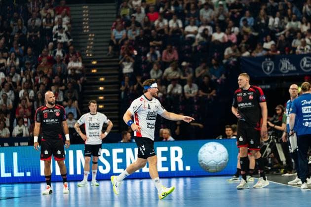 Adrian Sipos 8 MT Melsungen stands at the left edge of the picture, while a player of SG Flensburg Handewitt with 31 Emil Jakobsen and another Flensburg player with 4 act in the center of the scene In the background a filled audience can be seen MT Melsungen vs SG Flensburg Handewitt - EHF Finals Hamburg 2026 Copyright: xPhilippHeistx