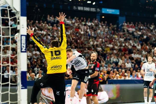 Nebojsa Simic 16 MT Melsungen stretches in goal and tries to save a throw from a Flensburg player Adrián Sipos 8 MT Melsungen stands in the background and watches the scene MT Melsungen vs SG Flensburg Handewitt - EHF Finals Hamburg 2026 Copyright: xPhilippHeistx