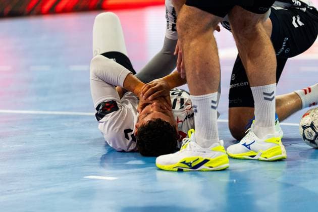 A player from SG Flensburg Handewitt lies on the floor in pain and holds his face A player from MT Melsungen kneels next to him and supports him MT Melsungen vs SG Flensburg Handewitt - EHF Finals Hamburg 2026 Copyright: xPhilippHeistx