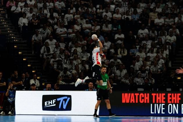 A player from SG Flensburg Handewitt jumps up and takes a shot, while a player from MT Melsungen stands in the background The EHF TV banner is visible in the foreground MT Melsungen vs SG Flensburg Handewitt - EHF Finals Hamburg 2026 Copyright: xPhilippHeistx