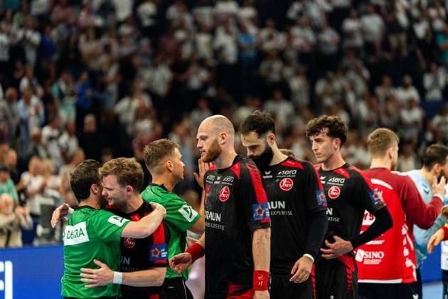 Several MT Melsungen players stand together on the pitch after the final whistle, Arnar Freyr Arnarsson 21 MT Melsungen can be seen in the center of the picture A referee in a green jersey hugs an MT Melsungen player MT Melsungen vs SG Flensburg Handewitt - EHF Finals Hamburg 2026 Copyright: xPhilippHeistx