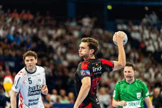 An MT Melsungen player takes a shot while Niclas Kirkeløkke 5 SG Flensburg Handewitt watches in the background A referee in a green jersey follows the scene MT Melsungen vs SG Flensburg Handewitt - EHF Finals Hamburg 2026 Copyright: xPhilippHeistx