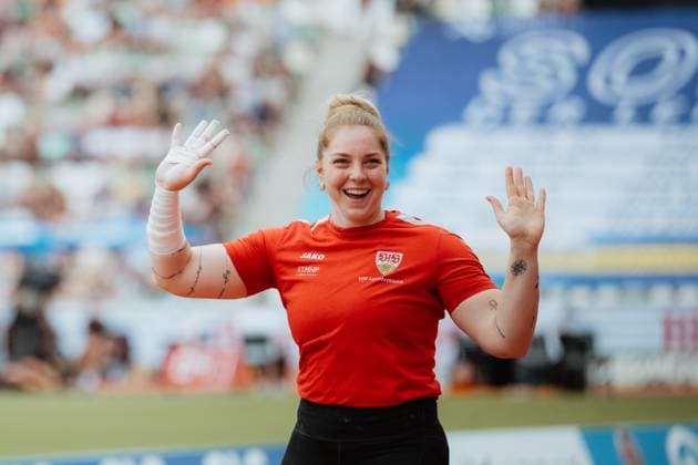 An athlete from VfB Leichtathletik celebrates in front of the crowd with her hands raised and a beaming smile She wears a red Jako jersey with the VfB Stuttgart crest and bandaged hand Athlete from VfB Leichtathletik cheers in the stadium Copyright: xspeedshotx xBeatricexBauerx