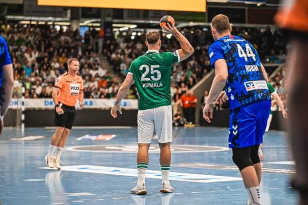 Player 25 Jurmala from Frisch Auf Göppingen prepares a throw while a defender 44 Rubin from TVB Stuttgart exerts pressure A referee in an orange jersey can be seen in the background Jurmala 25 Frisch Auf Göppingen preparing a throw against TVB Stuttgart Copyright: xspeedshotx xDorianfrickx