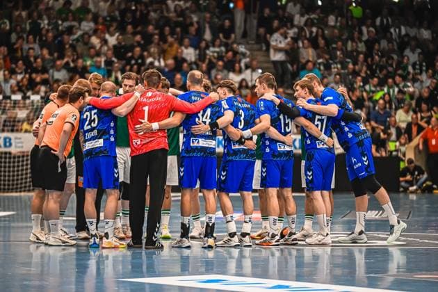 The TVB Stuttgart players form a team circle on the pitch, including 25 Zieker , 34, 3, 15 and 57 In the circle you can also see a player from Frisch Auf Göppingen in a green jersey and the goalkeeper in a red jersey TVB Stuttgart team circle in front of a sold-out crowd Copyright: xspeedshotx xDorianfrickx