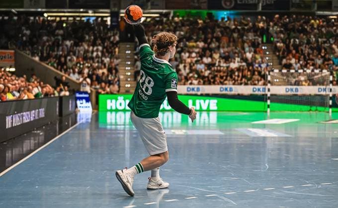 A Frisch Auf Göppingen player with the number 28 takes a shot and aims for the goal The packed hall forms the backdrop to the match scene Frisch Auf Göppingen player 28 taking a shot on goal Copyright: xspeedshotx xDorianfrickx