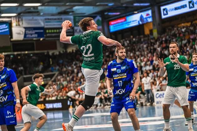 Player 22 Person from Frisch Auf Göppingen pulls up for a jump shot, while a player from TVB Stuttgart 17 organizes the defense In the background, other players from both teams follow the action in front of a sold-out crowd Person 22 Frisch Auf Göppingen taking a jump shot against TVB Stuttgart Copyright: xspeedshotx xDorianfrickx
