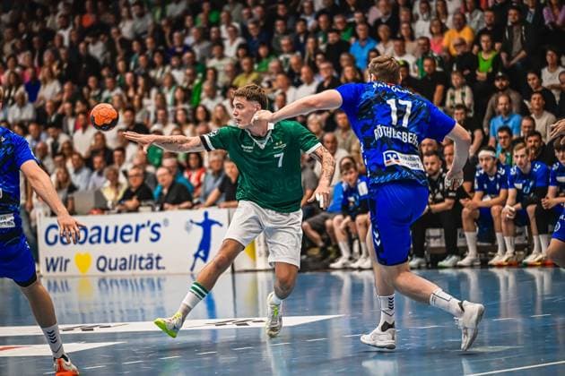 Kasper Lien 7 TVB Stuttgart, wearing a green jersey, pulls up to take a shot on goal while a Frisch Auf Göppingen player with the number 17 Röthlisberger tries to block the shot The handball is already in the air Kasper Lien 7 TVB Stuttgart taking a shot against Frisch Auf Göppingen Copyright: xspeedshotx xDorianfrickx