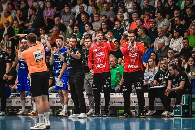 Two TVB Stuttgart players in red jerseys 21 and 16 gesticulate emotionally on the sideline next to coaches and trainers In the background you can see a referee in an orange jersey and a TVB player 10 in a blue jersey TVB Stuttgart players 21, 16 and coaches on the sideline Copyright: xspeedshotx xDorianfrickx