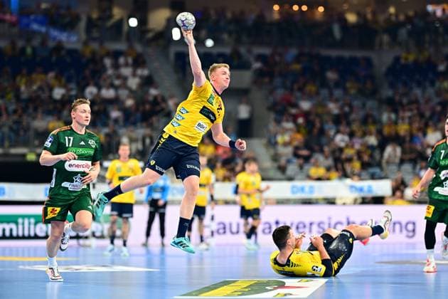 A Rhein Neckar Löwen player jumps high into the air and takes a throw, while August Baskar Pedersen 17 TSV Hannover Burgdorf runs along in the background Another Löwen player lies on the ground, a Hannover player with 7 can be seen on the right edge of the picture Rhein Neckar Löwen player jumps to throw against August Baskar Pedersen 17 TSV Hannover Burgdorf Copyright: xMichaelxGelhardtx