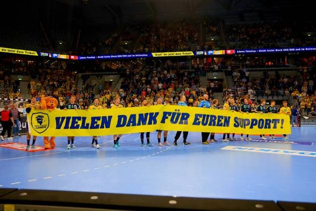 The Rhein Neckar Löwen players stand together with the mascot on the pitch after the game and hold a yellow banner with the words Thank you for your support in the background as the spectators applaud in the packed arena Rhein Neckar Löwen thank the fans with a banner Copyright: xspeedshotx