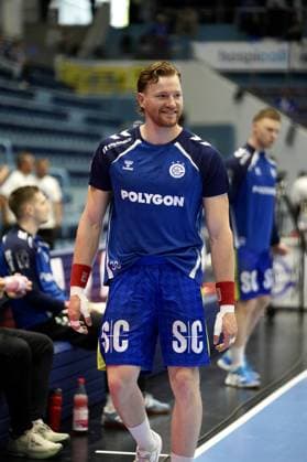 Tom Kiesler 30 VfL Gummersbach runs along the sideline smiling, with bandaged hands and red sweatbands Other VfL Gummersbach players and the team bench can be seen in the background Tom Kiesler 30 VfL Gummersbach on the sideline in the SCHWALBE arena Copyright: xspeedshotx xD.xBarndtx